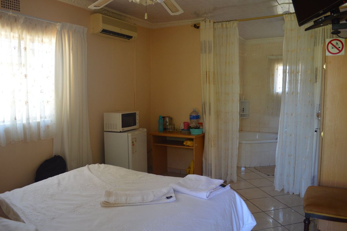 A bedroom suite featuring tiled flooring, a ceiling fan, wall-mounted air conditioning, and an integrated bathroom area with a built-in bathtub.