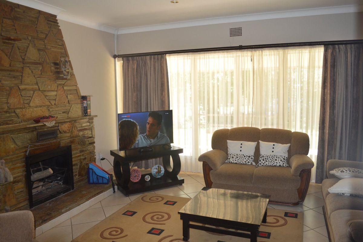 A living room featuring a prominent stone fireplace, tiled flooring, and large windows with curtain tracks, offering a comfortable and functional space.