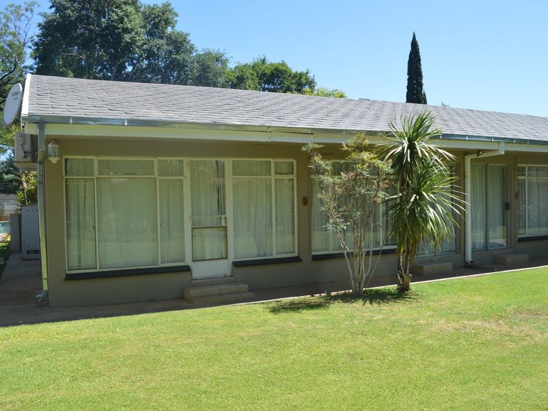 Rear view of a commercial property featuring a pitched shingle roof, large aluminium-framed windows, and a well-maintained lawn area.
