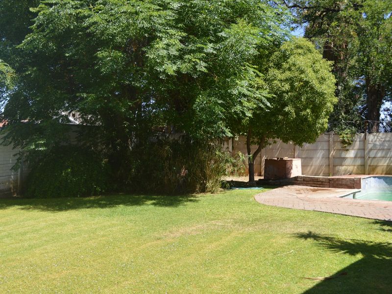 Outdoor pool area featuring a swimming pool, brick paved surround, and a built-in barbecue area set within a garden with mature trees.