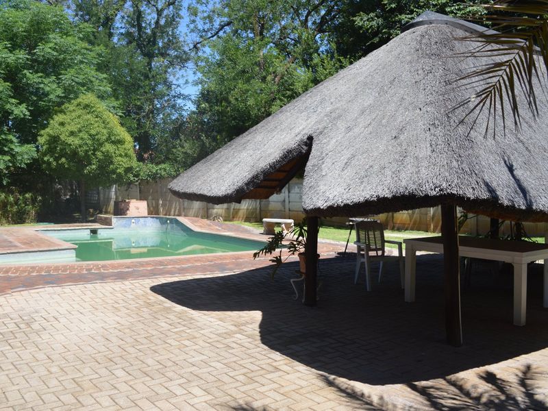 Outdoor entertainment area featuring a swimming pool and a traditional thatched lapa structure set within a garden space.