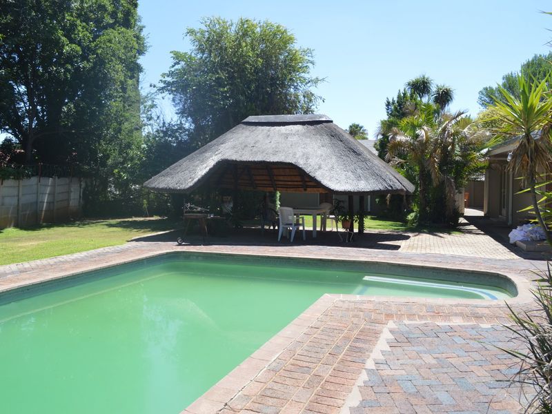 Outdoor pool area featuring a traditional thatch lapa, brick paved surround, and established garden setting.