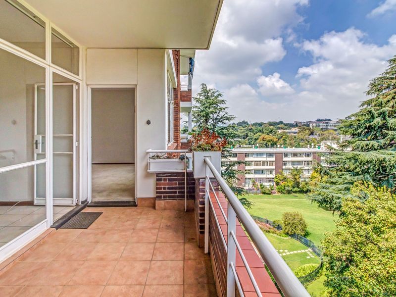A spacious balcony featuring tiled flooring and a metal railing, offering pleasant views of the surrounding garden and neighborhood.