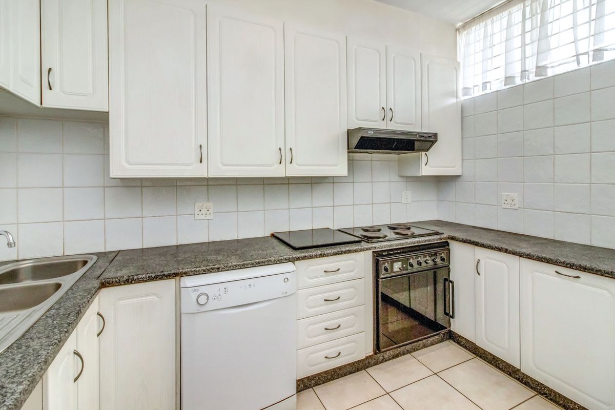 A functional kitchen featuring white cabinetry, granite countertops, a built-in electric stove with extractor fan, and tiled finishes throughout.