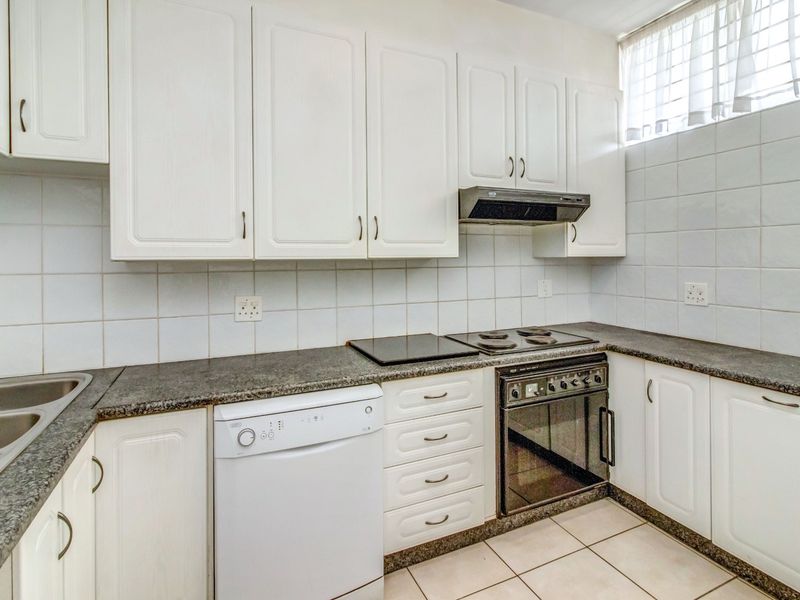 A functional kitchen featuring white cabinetry, granite countertops, a built-in electric stove with extractor fan, and tiled finishes throughout.
