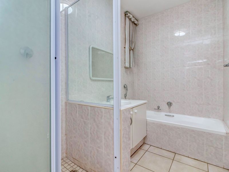 A functional bathroom featuring a bathtub, separate shower enclosure, and a vanity cabinet with a basin, finished with neutral wall and floor tiles.
