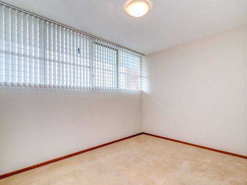 A clean, empty bedroom featuring neutral carpeting, vertical blinds, and a simple ceiling light fixture, providing a blank canvas for personalization.