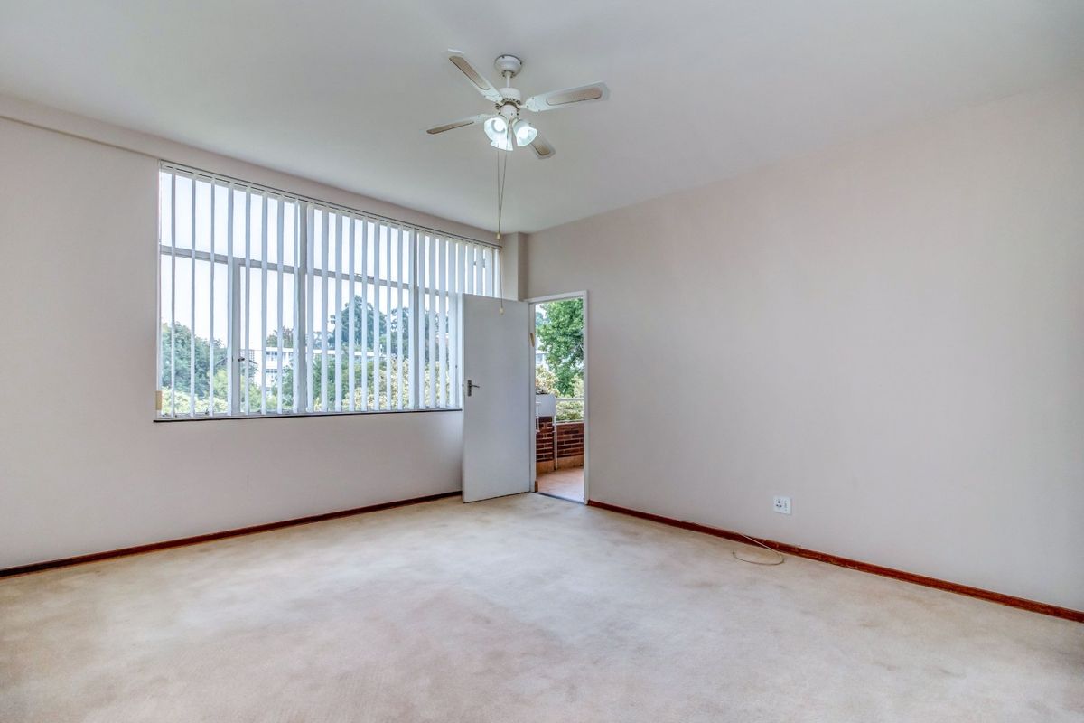 An empty bedroom featuring carpet flooring, a ceiling fan, and a large window with vertical blinds, offering access to an outdoor balcony area.