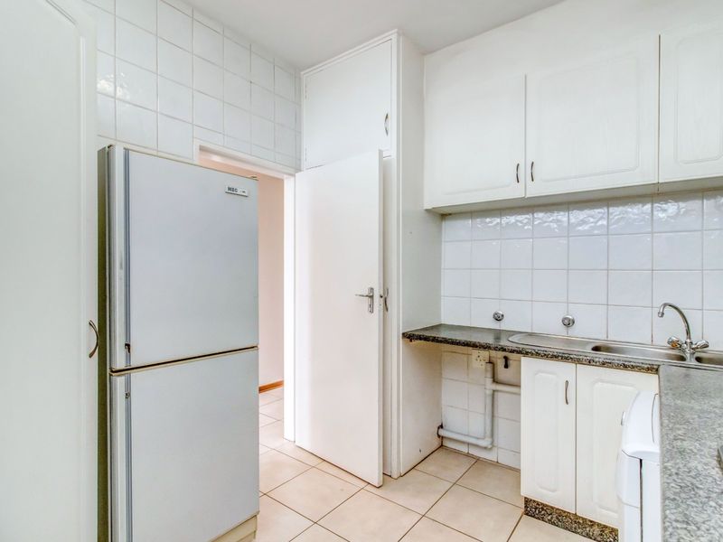 A functional kitchen featuring white built-in cabinetry, laminate countertops, a stainless steel sink, and tiled backsplash with neutral floor tiles.