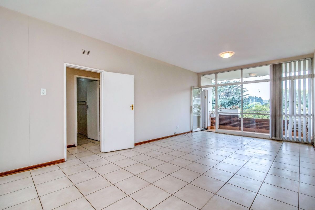 Spacious, light-filled living area featuring neutral tiled flooring and large glass doors leading to an outdoor balcony.