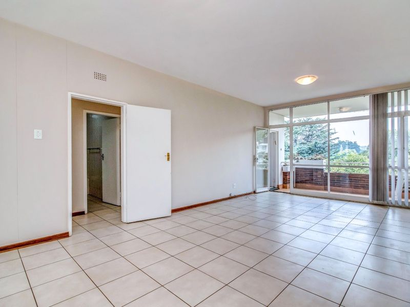 Spacious, light-filled living area featuring neutral tiled flooring and large glass doors leading to an outdoor balcony.