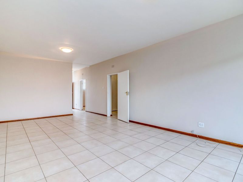 A spacious, empty living area featuring neutral ceramic floor tiles, clean walls, and standard interior door access to adjacent rooms.