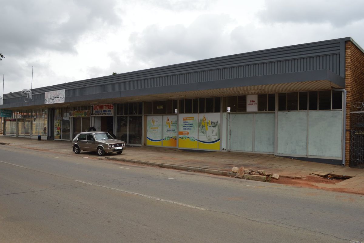 Street-level view of a commercial retail strip building featuring large glass storefronts and a metal corrugated fascia.