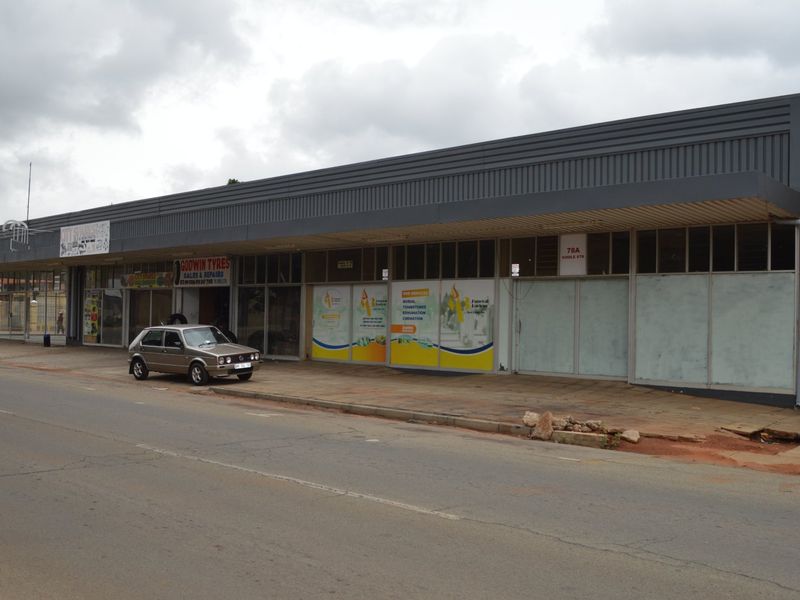 Street-level view of a commercial retail strip building featuring large glass storefronts and a metal corrugated fascia.