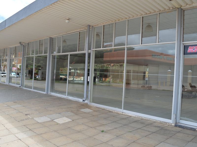 Commercial storefront featuring extensive glass display windows, aluminum framing, and a covered paved walkway entrance.