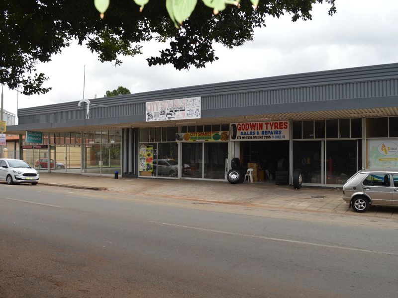 Street-level view of a commercial retail strip center featuring multiple storefronts with large glass windows and metal signage fascias.
