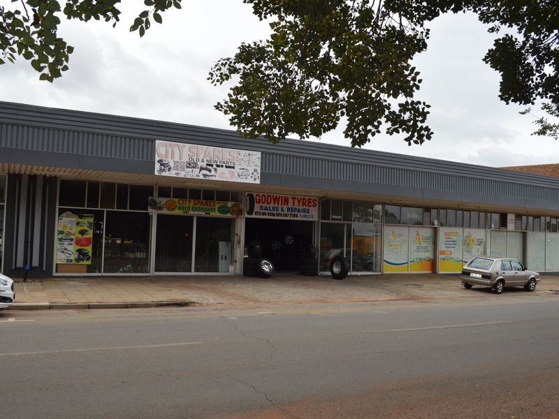 Front exterior view of a commercial retail strip building featuring large glass storefronts and metal facade cladding along a street.
