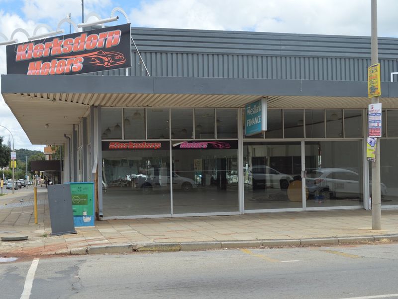 Commercial storefront property featuring a large glass display area, metal facade cladding, and prominent signage, situated on a paved street corner.