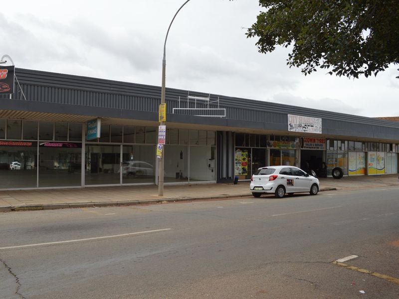 Street-level view of a commercial retail strip with large glass storefronts and metal facade cladding.