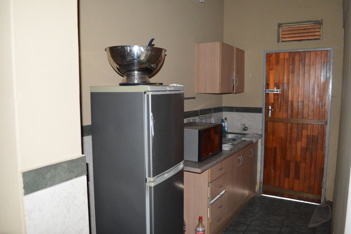 A compact kitchen area featuring built-in cabinetry, laminate countertops, a stainless steel sink, and a timber door with a ventilation louvre.