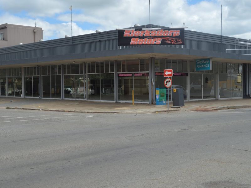 A corner commercial property featuring extensive glass display windows and metal facade cladding, situated at a prominent street intersection.