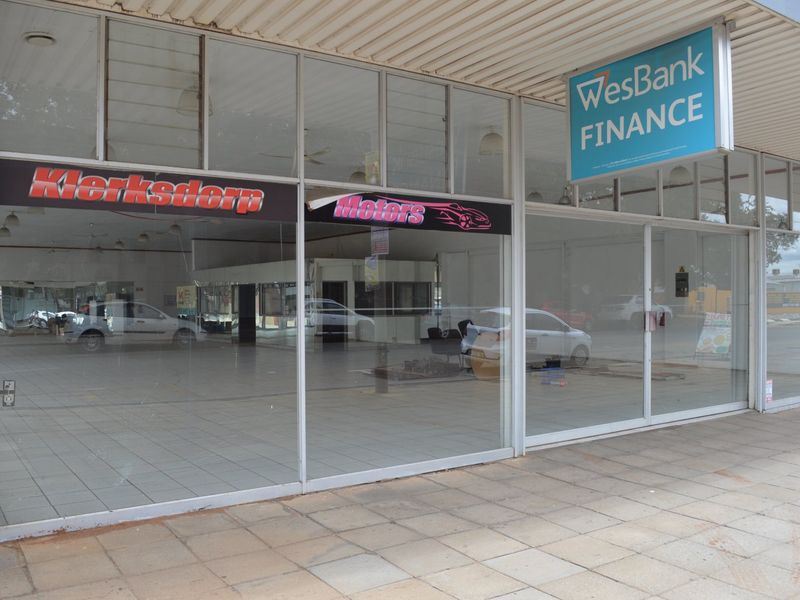 Commercial storefront featuring large glass display windows, tiled flooring, and a covered paved walkway entrance.