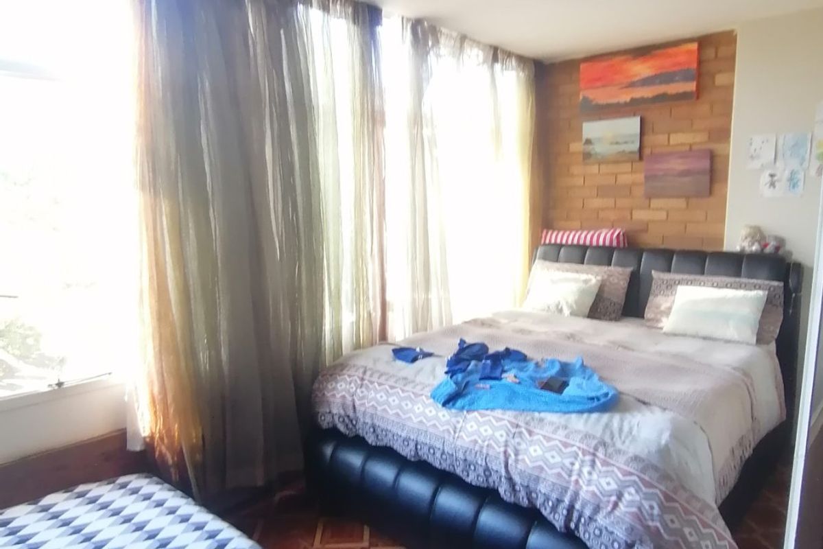 A bedroom featuring an exposed brick accent wall, tiled flooring, and large windows allowing for ample natural light.