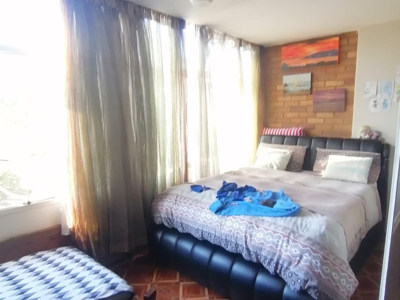 A bedroom featuring an exposed brick accent wall, tiled flooring, and large windows allowing for ample natural light.