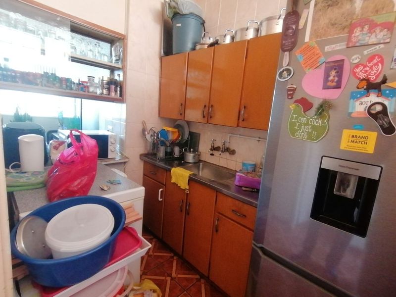 A compact kitchen featuring dated wooden cabinetry, a stainless steel sink, and tiled finishes, offering potential for a modern renovation.