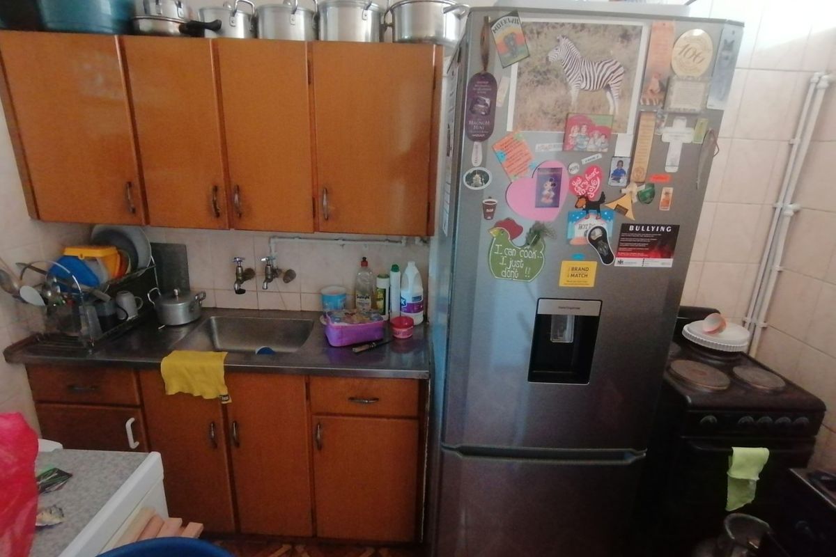 A compact kitchen featuring dated wooden cabinetry, a stainless steel sink, and tiled finishes, offering potential for a modern renovation.