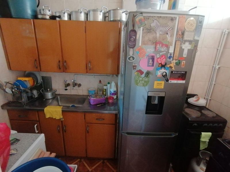 A compact kitchen featuring dated wooden cabinetry, a stainless steel sink, and tiled finishes, offering potential for a modern renovation.