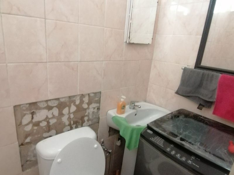 Compact bathroom featuring a pedestal basin and toilet, currently requiring repair to the wall tiling and plasterwork.