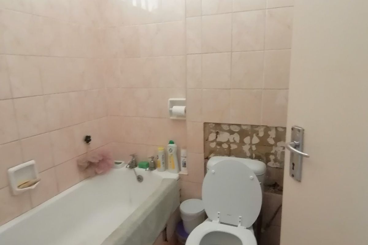 A dated bathroom featuring a bathtub and toilet, currently requiring repairs to the wall tiling behind the toilet area.
