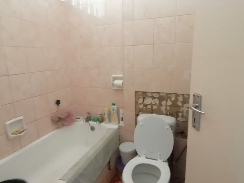A dated bathroom featuring a bathtub and toilet, currently requiring repairs to the wall tiling behind the toilet area.