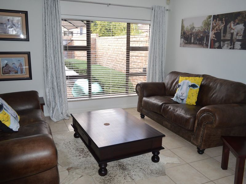 A comfortable living room featuring tiled flooring and a large window with venetian blinds, providing natural light and a view of the rear garden.