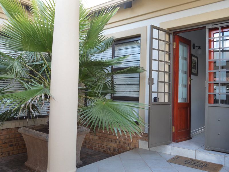 A covered patio area featuring tiled flooring, a security gate, and a timber entrance door, providing a secure and welcoming transition into the home.