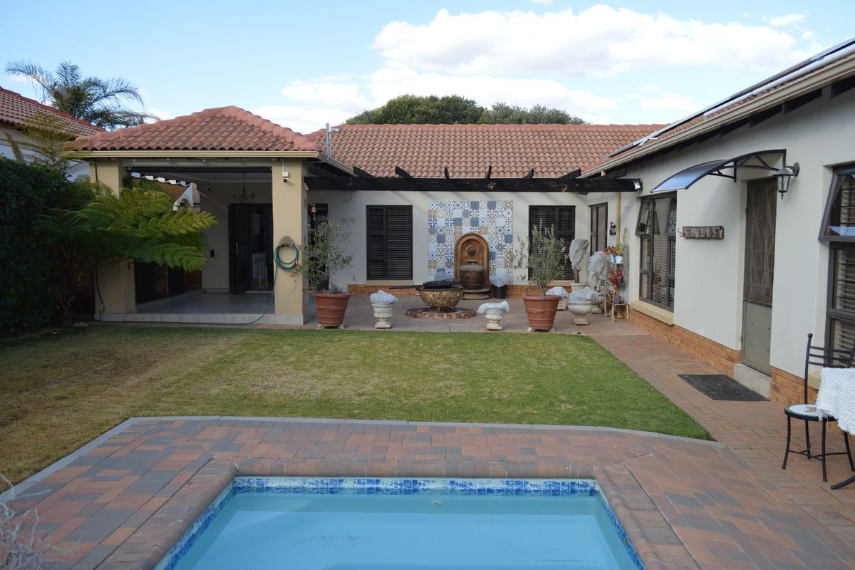 Rear exterior view featuring a swimming pool, paved patio area, covered veranda, and a landscaped garden with a decorative water feature.
