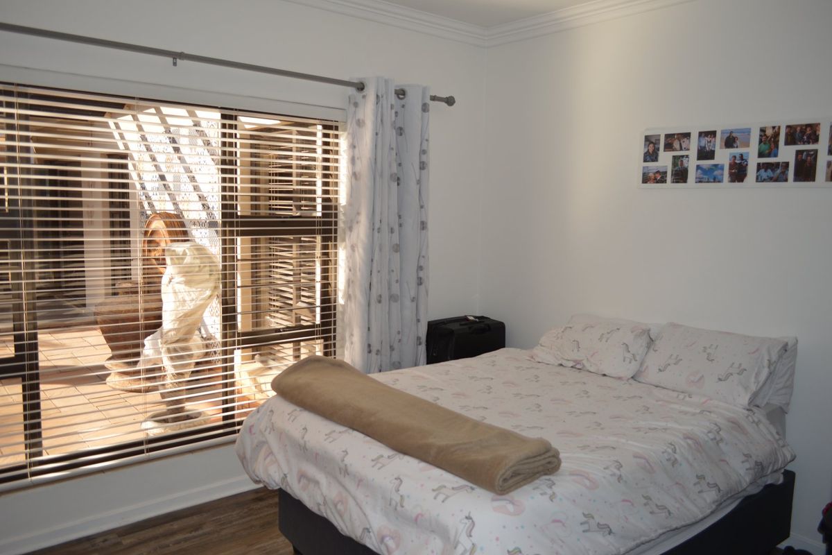 A well-maintained bedroom featuring laminate flooring, coving, and large windows with venetian blinds and curtain rods, offering natural light and access to an outdoor area.