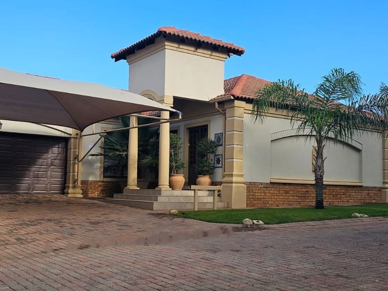 Front elevation of a well-maintained house featuring a paved driveway, shade sail, double garage, and a covered entrance with architectural columns.