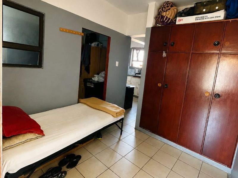 A bedroom featuring tiled flooring and built-in wooden cupboards, providing functional storage space within the apartment.