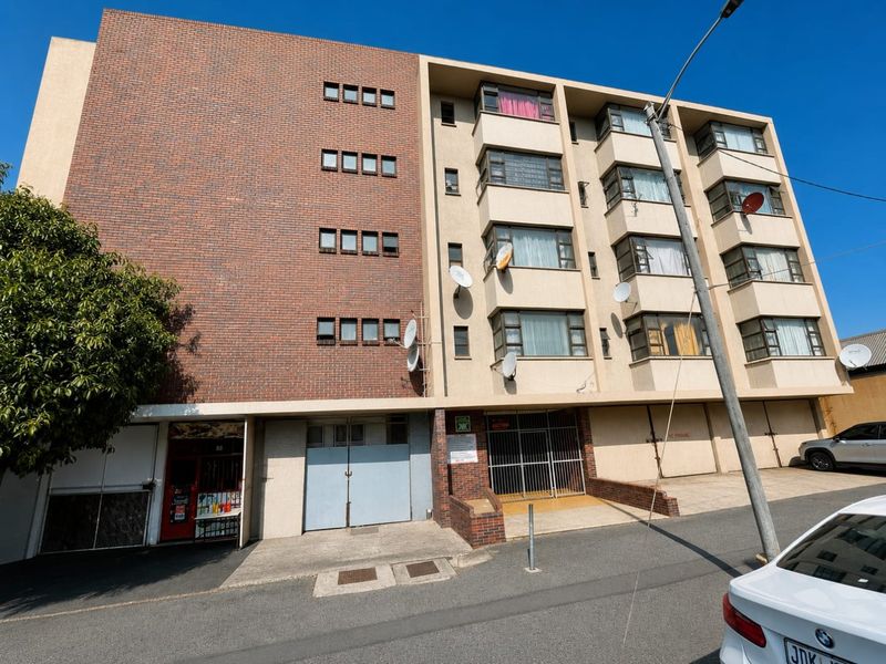 Front elevation of a multi-story apartment building featuring a brick facade, metal security gates, and multiple satellite dish installations.