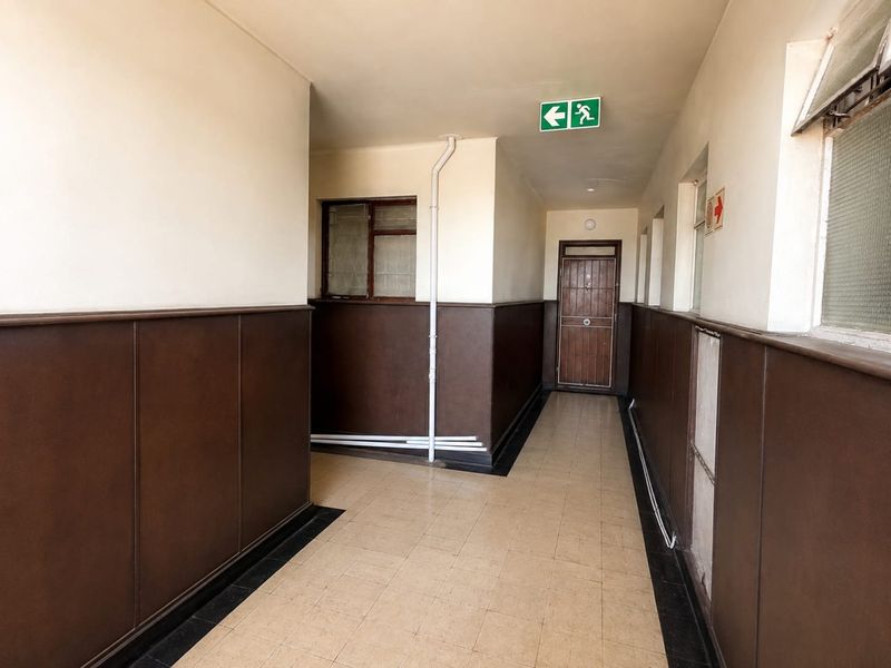 A functional apartment hallway featuring tiled flooring, wooden wainscoting, and standard access doors, providing a clean but dated circulation space.