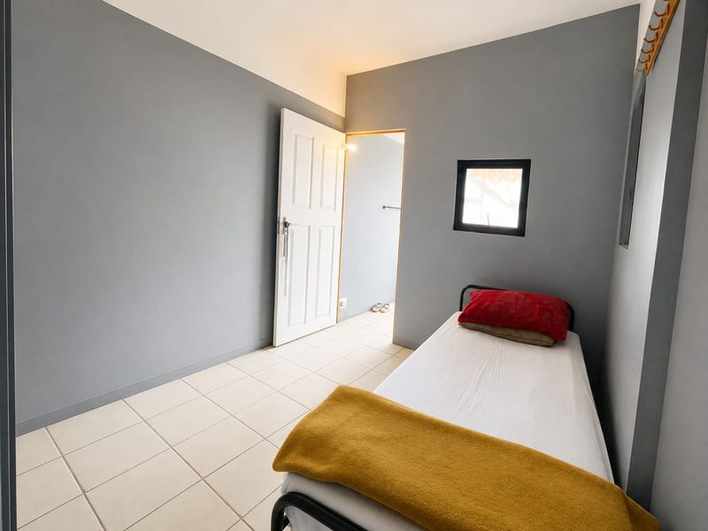 A compact bedroom featuring neutral grey walls, tiled flooring, and a small window, providing a simple and functional living space.