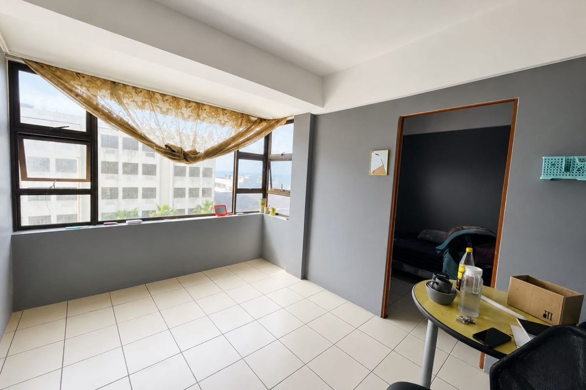 A bright, open-plan living area featuring neutral tiled flooring and large windows that provide ample natural light and urban views.
