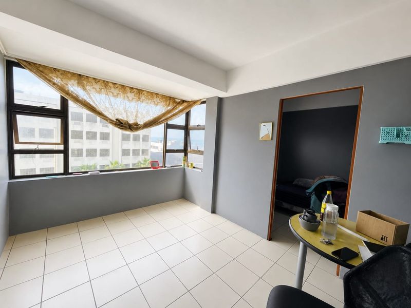A bright, open-plan living area featuring neutral tiled flooring and large windows that provide ample natural light and urban views.