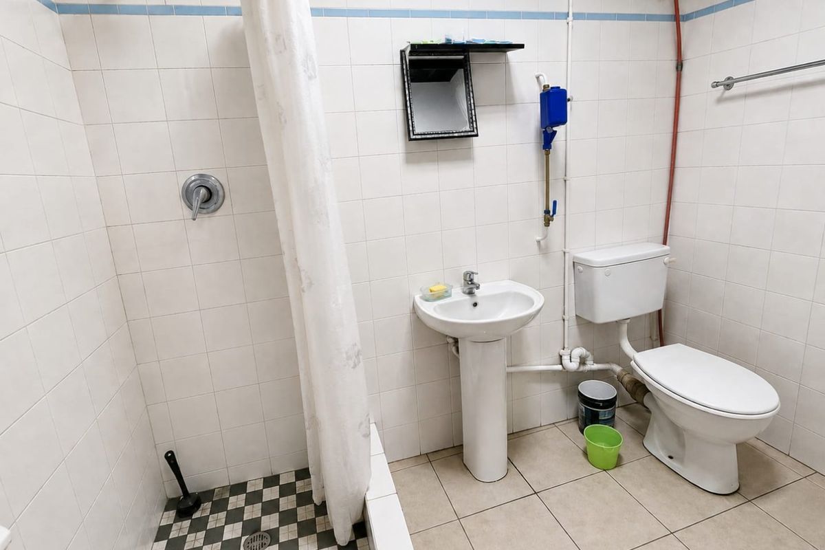 A functional bathroom featuring a pedestal washbasin, toilet, and shower area with tiled finishes and exposed plumbing.