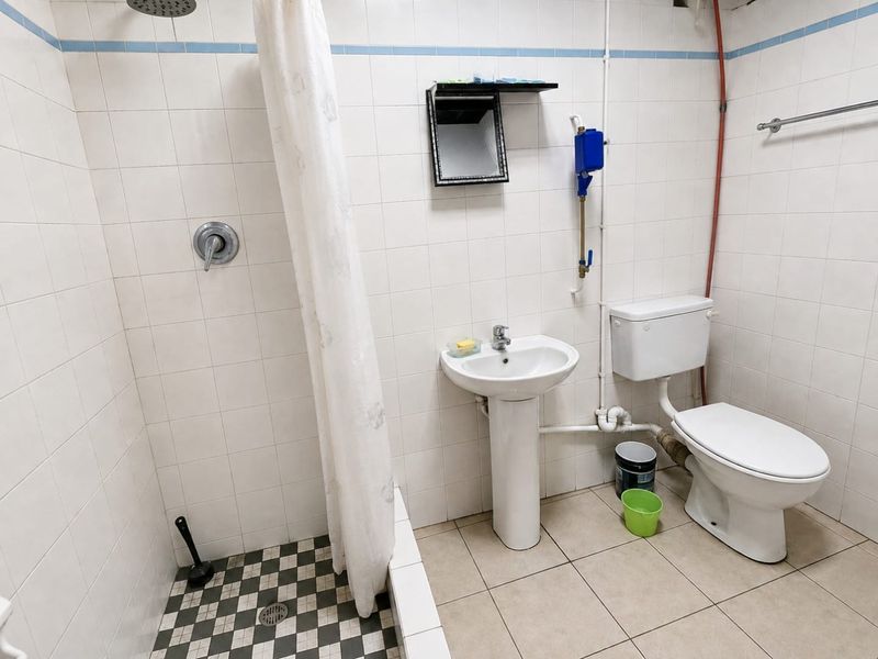 A functional bathroom featuring a pedestal washbasin, toilet, and shower area with tiled finishes and exposed plumbing.
