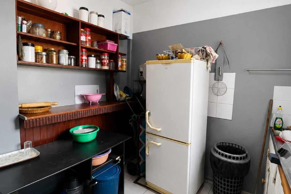 A functional kitchen area featuring tiled flooring, built-in wooden shelving, and a tiled splashback, offering potential for modernization and improved layout.