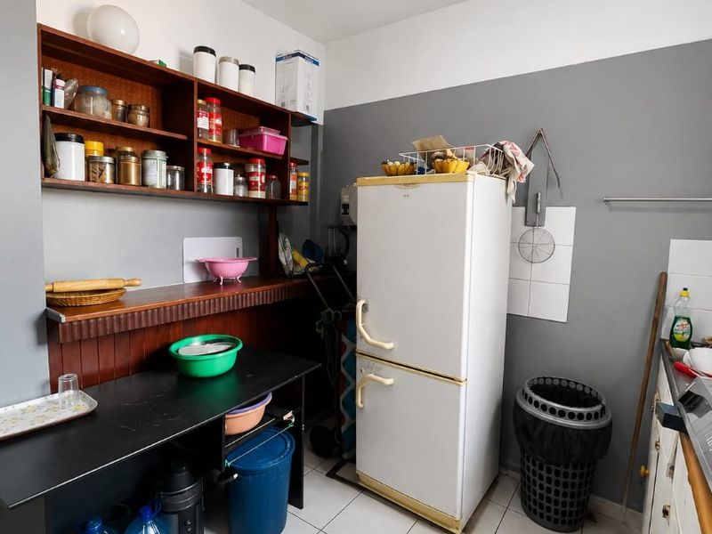A functional kitchen area featuring tiled flooring, built-in wooden shelving, and a tiled splashback, offering potential for modernization and improved layout.