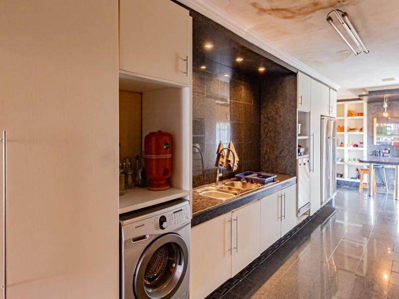 A functional scullery area featuring built-in cabinetry, granite countertops, and a double sink, with visible ceiling water damage requiring repair.